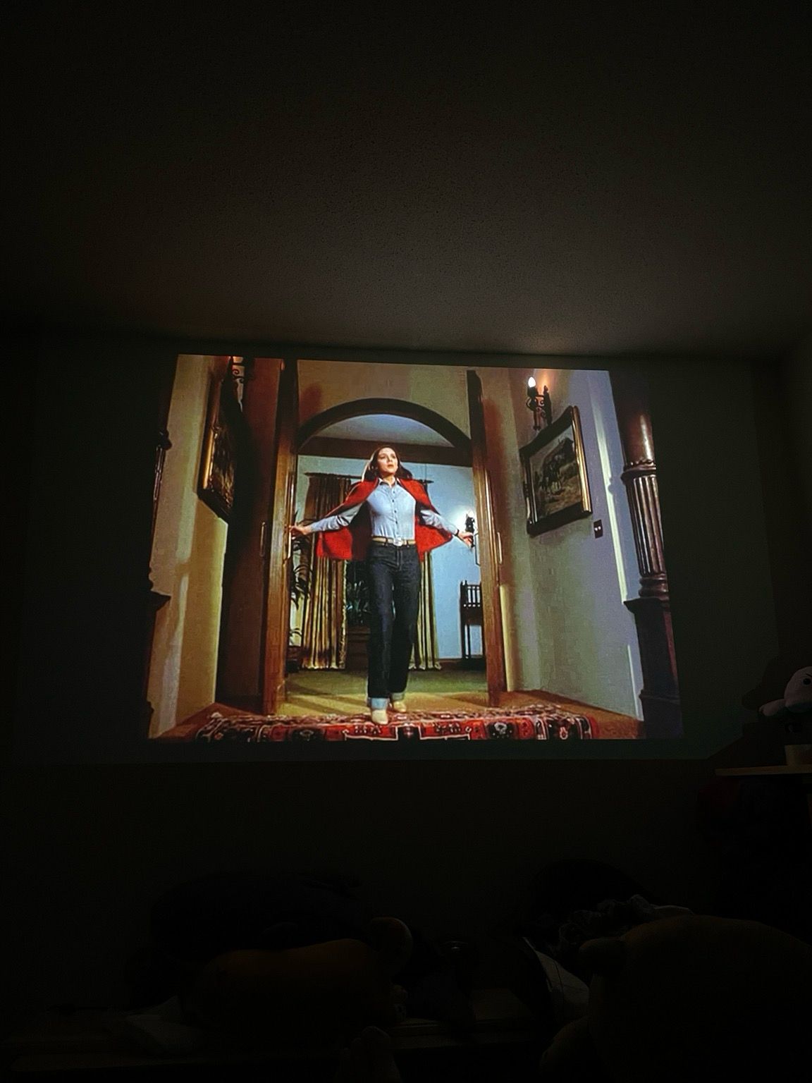 Photo showing a projector screen, woman in jeans and shirt, entering a room through double doors 